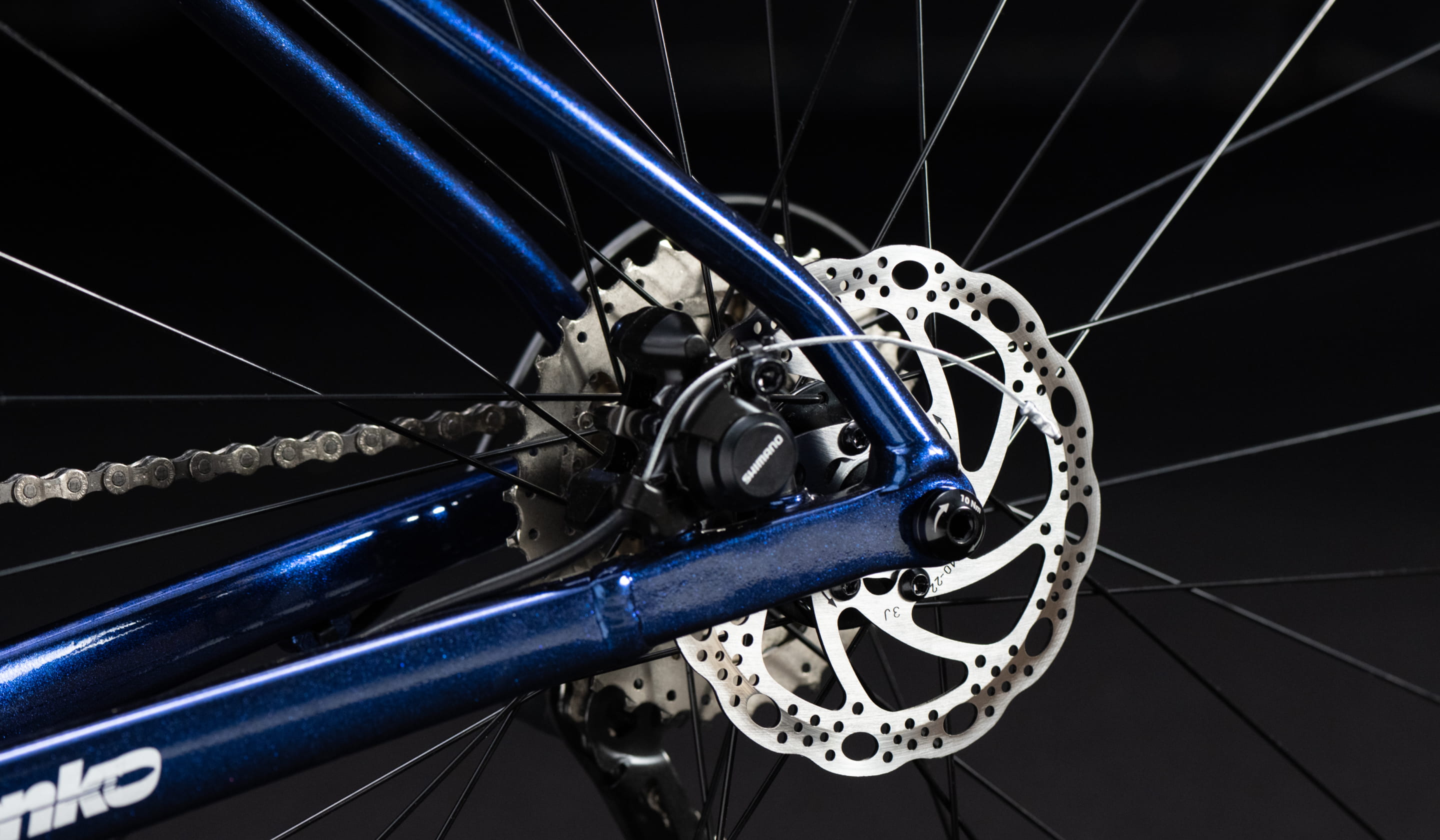 黒い背景に、ロードバイクのハンドルとフロント部分が強調された構図の写真。青とシルバーのフレームに、カーボンハンドルバーやディスクブレーキが特徴的で、スポーティかつ洗練されたデザインが際立つ。